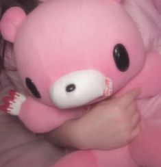 a pink teddy bear with black eyes laying on top of a person's arm