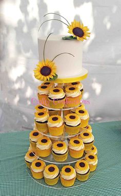 a tiered cake with sunflowers on top and cupcakes in the bottom