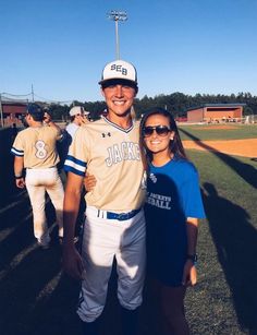 a man and woman are posing for a photo at a baseball game in the sun