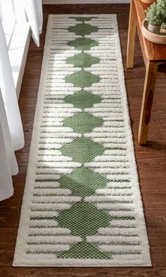 a green and white rug on the floor next to a wooden table with a potted plant