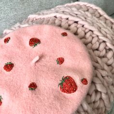 a pink hat with strawberries on it and a white knitted blanket next to it