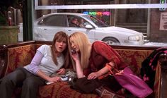 two women sitting on a couch in front of a car talking on the phone and one holding a purse