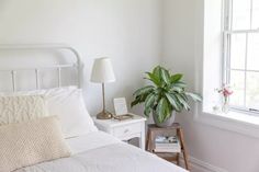 a bed with white sheets and pillows next to a potted plant in a window sill