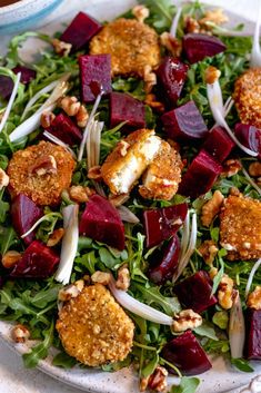 a salad with beets, carrots and nuts on a white plate next to a cup of tea