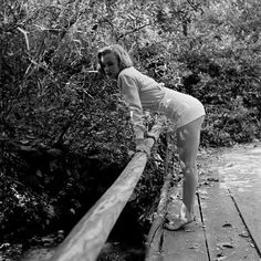 black and white photograph of a woman leaning on a wooden railing in front of trees