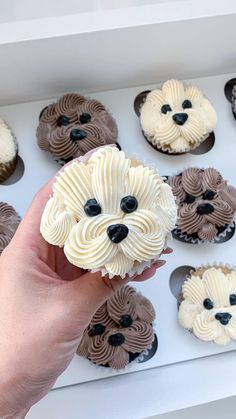 a person holding a cupcake with icing in front of some dog faces on it