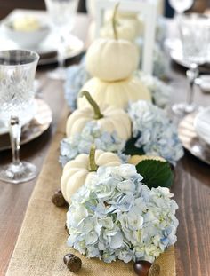 the table is set with white pumpkins and blue hydrangeas, as well as candles