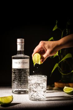 a person is squeezing a lemon into a glass with ice and limes around it