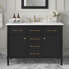 a bathroom vanity with marble counter top and gold hardware pulls on the cabinet, along with a black framed mirror above it