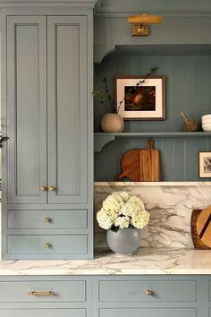 a kitchen with blue cabinets and marble counter tops, white flowers in a vase on the counter