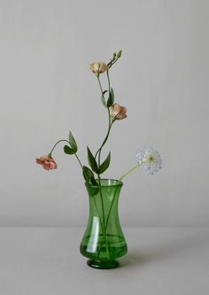 a green vase filled with flowers on top of a table