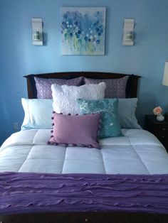 a bed with purple and blue pillows on top of it in a room that has two pictures above the headboard