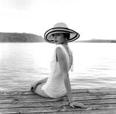 a woman sitting on a dock wearing a hat