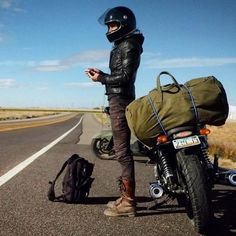 a person standing next to a motorcycle on the side of the road looking at their cell phone