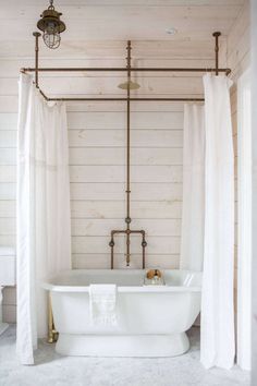 a white bath tub sitting under a bathroom window next to a shower curtain and light fixture