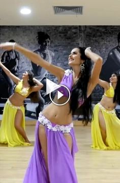 a woman in a purple and yellow dress dancing on a wooden floor with other dancers behind her