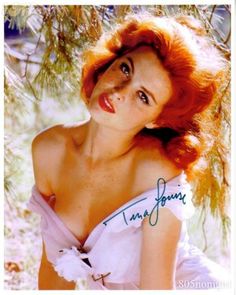 a woman with red hair wearing a white dress and posing in front of a tree