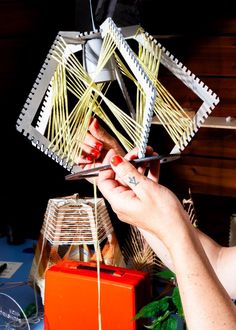 a woman is making a sculpture out of string and wood sticks on a table with other items