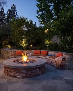 an outdoor fire pit surrounded by brick walls and seating around it at night with trees in the background