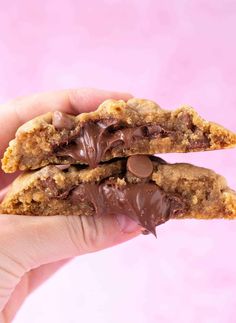 two chocolate chip cookies in the palm of someone's hand on a pink background