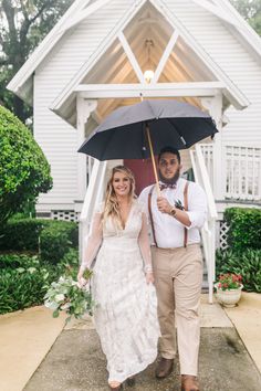 a bride and groom holding an umbrella in front of a white church with red door