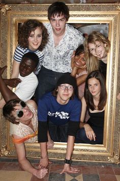 a group of people posing in front of a gold framed photo with one man looking at the camera