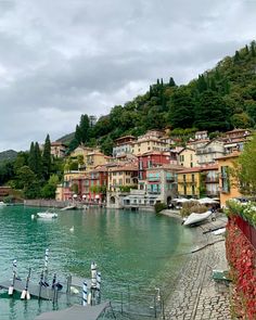 boats are parked on the water in front of some buildings and trees with mountains in the background