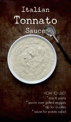 a white bowl filled with sauce sitting on top of a wooden table next to a spoon