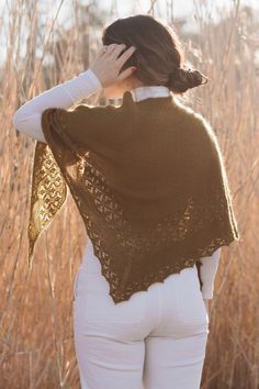 a woman in white pants and a brown shawl is standing near some tall grass