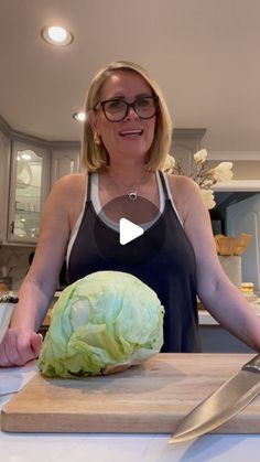 a woman standing in front of a cutting board with a cabbage on it