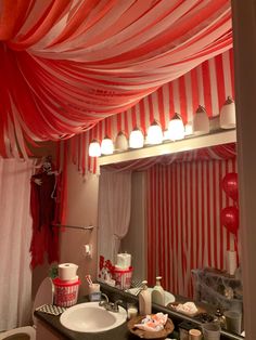 a bathroom decorated in red and white with striped drapes on the ceiling above the sink