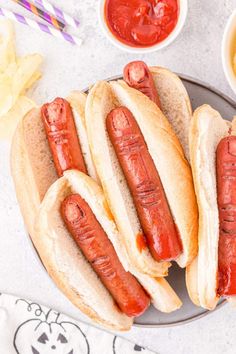 three hot dogs on buns with ketchup, mustard and relish in bowls