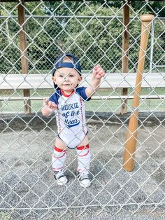 a little boy that is standing in front of a fence with a baseball uniform on