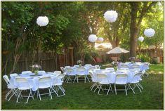 tables and chairs are set up in the yard for an outdoor party with white paper lanterns