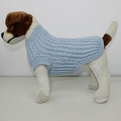 a stuffed dog wearing a blue sweater on top of a white table next to a wall