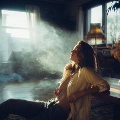 a woman sitting on a bench in front of a window with steam coming out of it