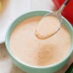 a spoon full of soup in a green bowl with a red container on the side