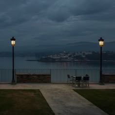 a couple of lights that are on some grass by the water and buildings in the background