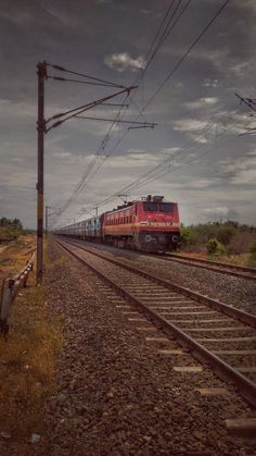 a red train traveling down tracks next to a field and power lines on a cloudy day