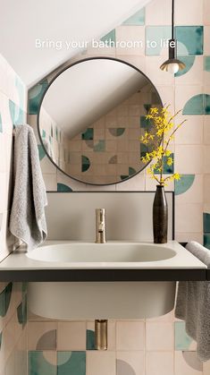 a bathroom sink under a round mirror next to a vase with yellow flowers in it