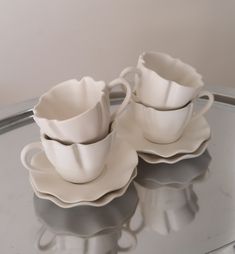 two white cups and saucers sitting on top of a glass table