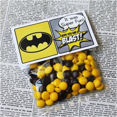 batman candy in a bag with yellow and black candies next to it on top of a newspaper