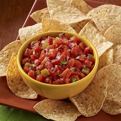 a yellow bowl filled with salsa surrounded by tortilla chips on a red plate