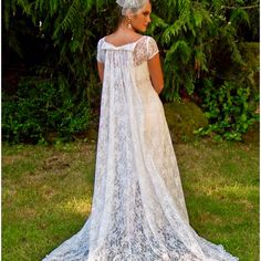 a woman in a white dress and veil standing on the grass with her back to the camera