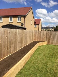 a wooden garden bed in front of a brick house with grass and dirt on the ground