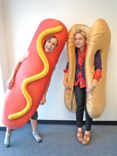 two women standing next to each other with giant hot dogs in the shape of buns