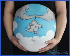 a pregnant woman's belly with an elephant painted on it, and clouds in the background