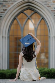 a woman sitting on the ground with her graduation cap in front of an arched window