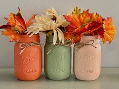 three mason jars with fall leaves and flowers in them