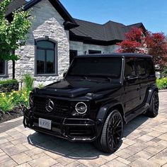 a black mercedes g - class is parked in front of a house with brick driveway